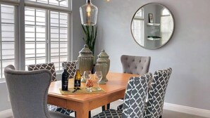 Un espace repas comprenant une table en bois, des chaises à revêtement gris et des luminaires suspendus.