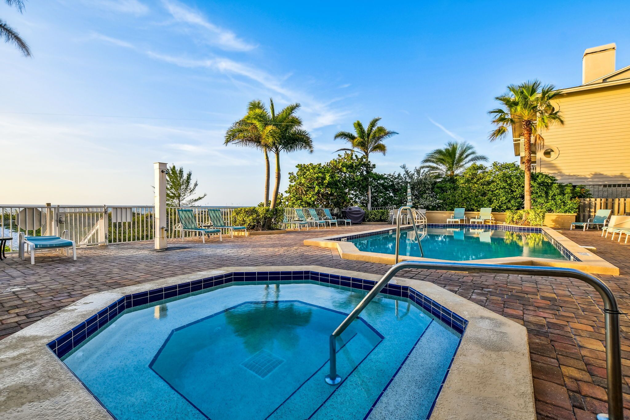 A rooftop pool area with two pools, lounge chairs, and palm trees.