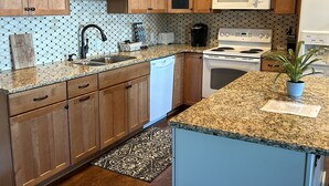 A modern kitchen with wooden cabinets, a granite countertop, a microwave, a stove, and a dishwasher.