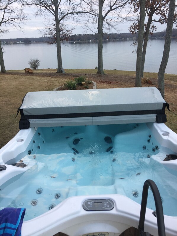 A hot tub with a control panel, surrounded by trees and a view of a lake.