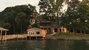 A large, multi-story house with a stone dock extending into a body of water, surrounded by trees.
