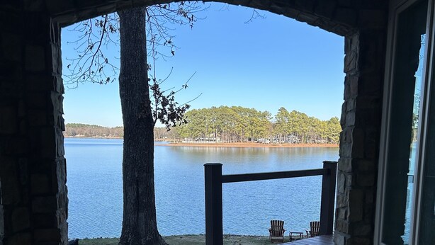 A stone archway leading to a deck with a view of a lake and trees.