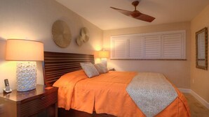 A bedroom with a bed, two wall clocks, a ceiling fan, and a bedside table with a lamp and a phone. - Kuhio Shores 306:  Vacation On Kauai Oceanfront (Poipu)