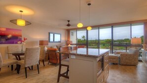A spacious living area with a large window, a dining table, and several chairs. - Kuhio Shores 306:  Vacation On Kauai Oceanfront (Poipu)