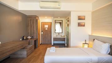 A hotel room with a wooden desk, a bed with white linens, a bathroom with a sink and mirror, and a wall-mounted air conditioner.