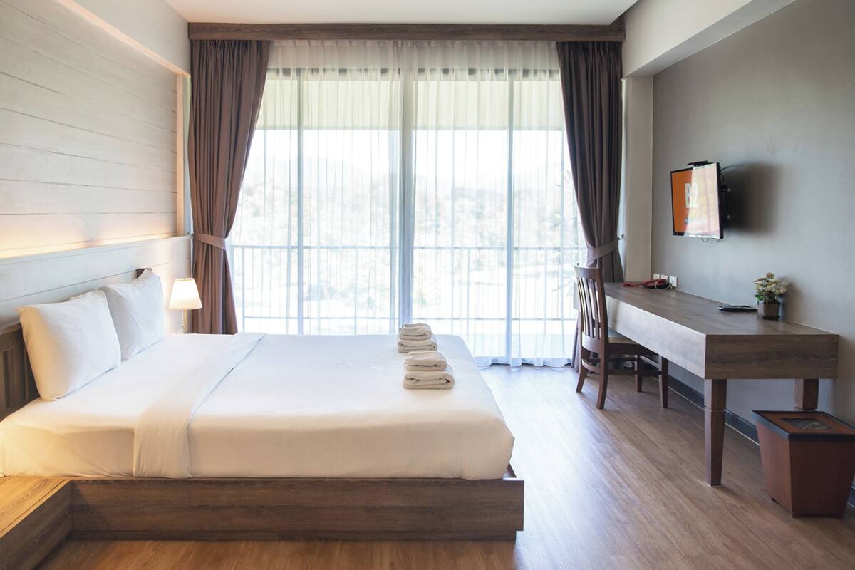Ein Hotelzimmer mit Bett, Nachttisch, Lampe, Schreibtisch, Stuhl und Fernseher an der Wand.