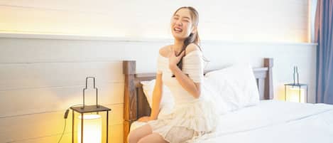 A person sitting on a bed in a room with wooden paneling, a nightstand with a lamp, and a wall-mounted light fixture.