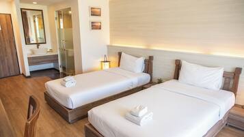A hotel room with two beds, a wooden floor, a bathroom with a mirror, and a small plant on the bedside table.