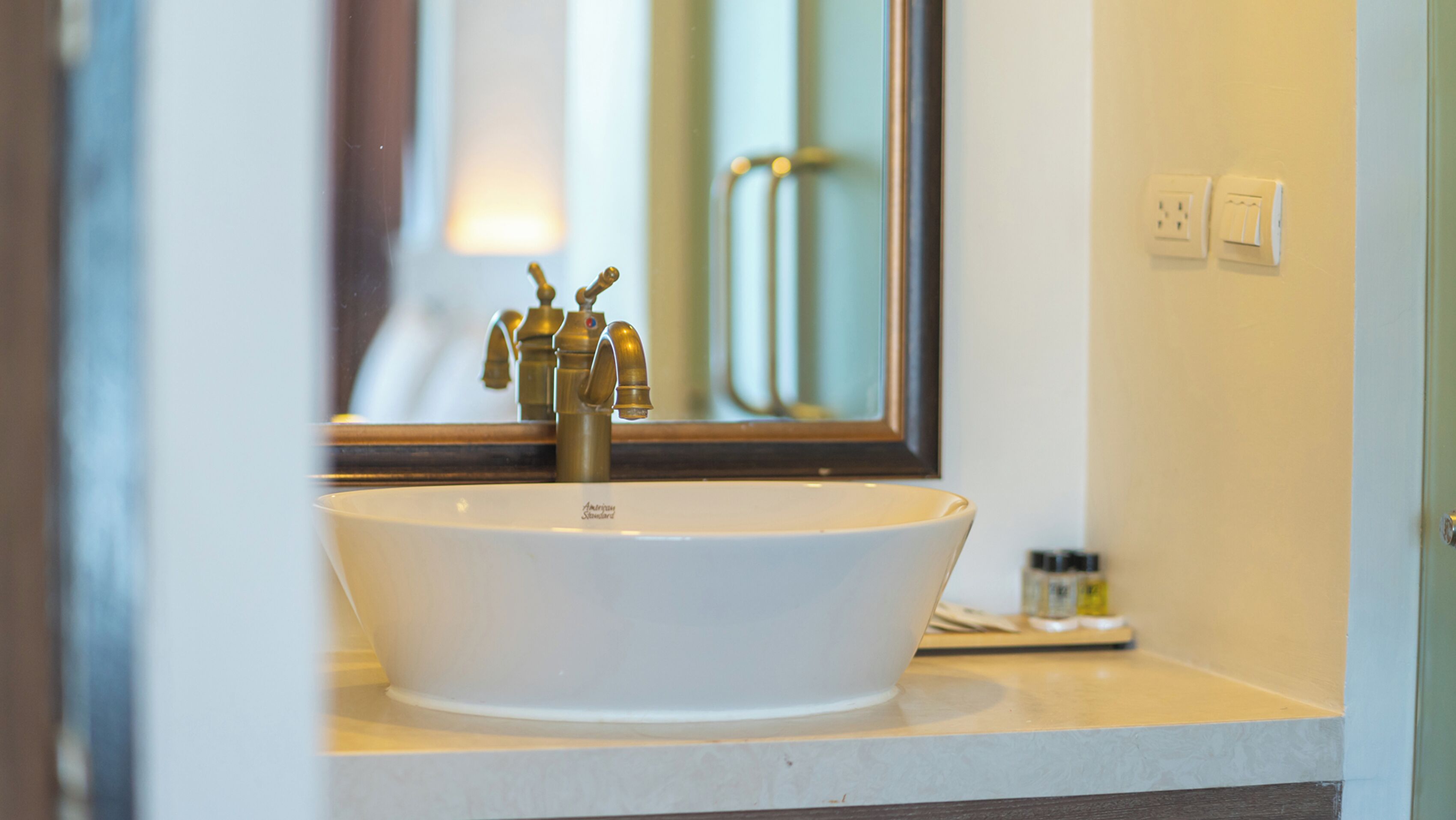 A white vessel sink with a single faucet, a mirror above it, and a small shelf with toiletries.