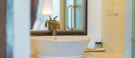 A white vessel sink with a single faucet, a mirror above it, and a small shelf with toiletries.