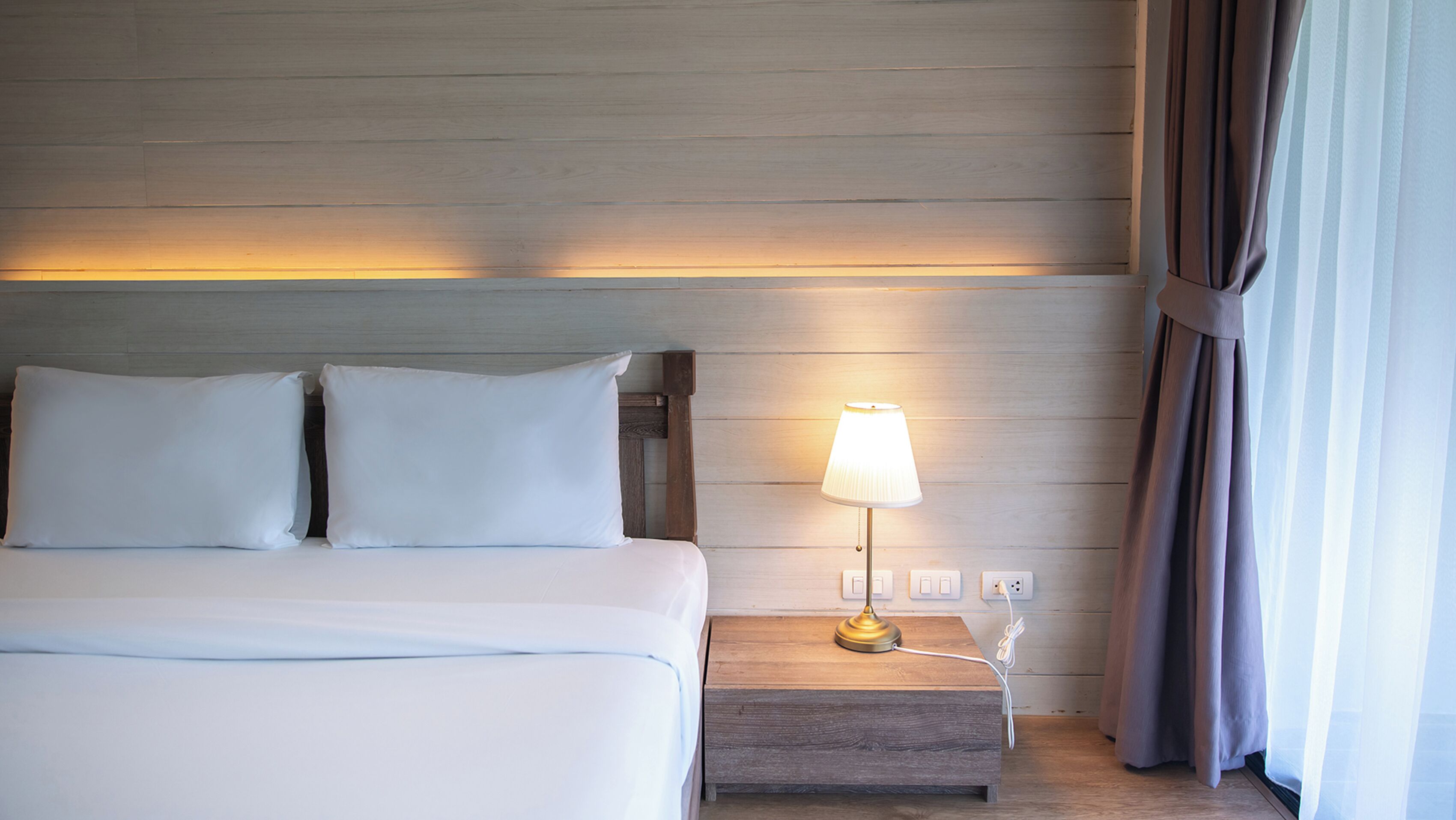 A hotel room with a bed, a nightstand with a lamp, and a power outlet.