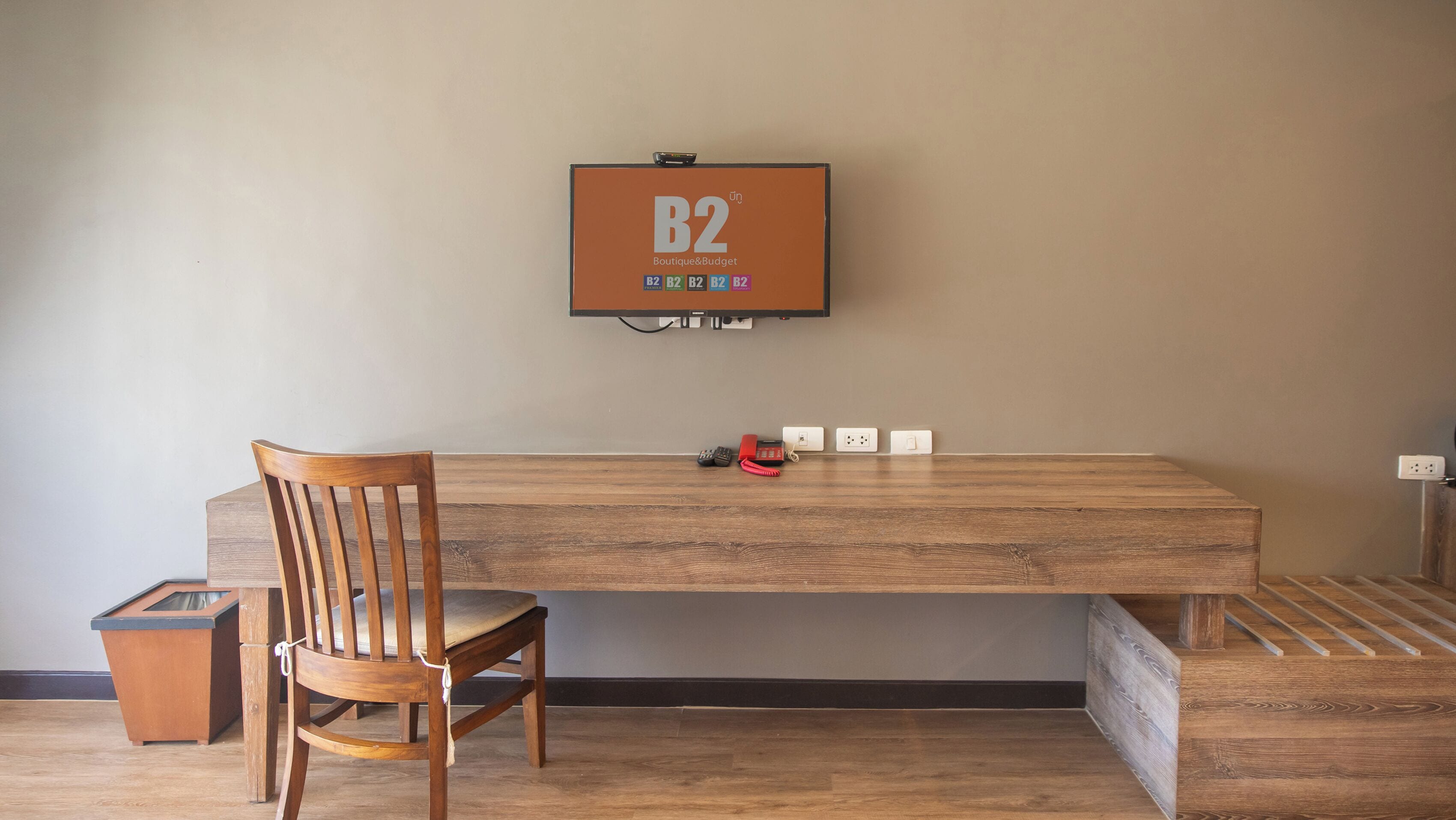 A wooden desk with a chair, a wall-mounted power outlet, and a framed sign with 'B2 Boutique & Budget' on a plain wall.
