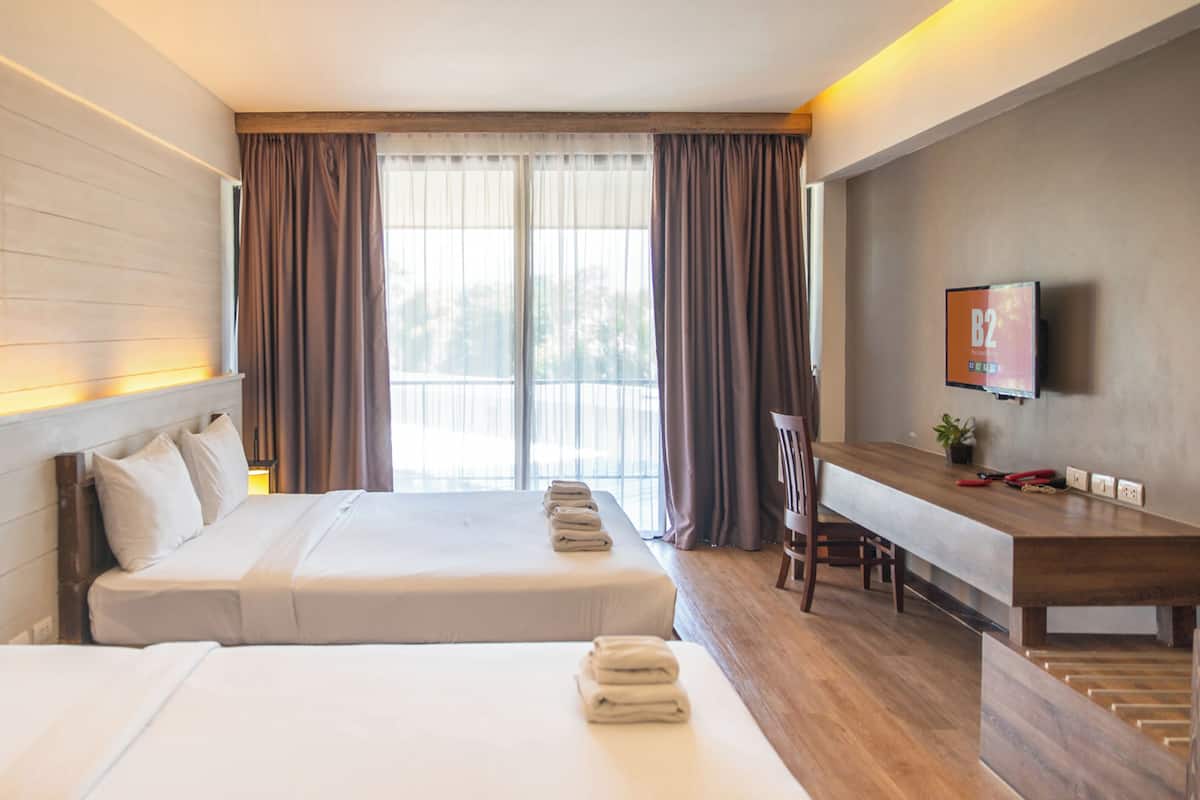 Ein Hotelzimmer mit zwei Betten, einem Schreibtisch, einem Stuhl, einem Fernseher und einem Fenster mit Vorhängen.