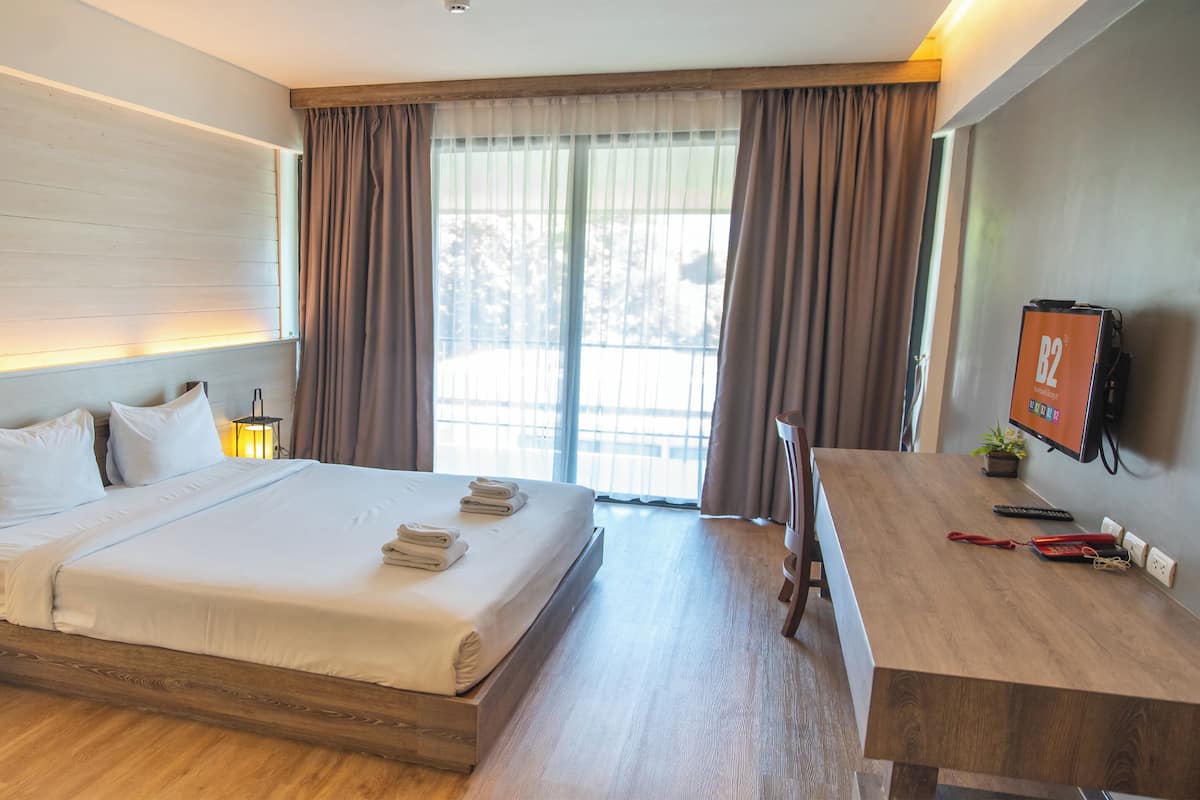 Ein Hotelzimmer mit Bett, Nachttischlampen, einem Schreibtisch mit Fernseher und einem Vorhangfenster.