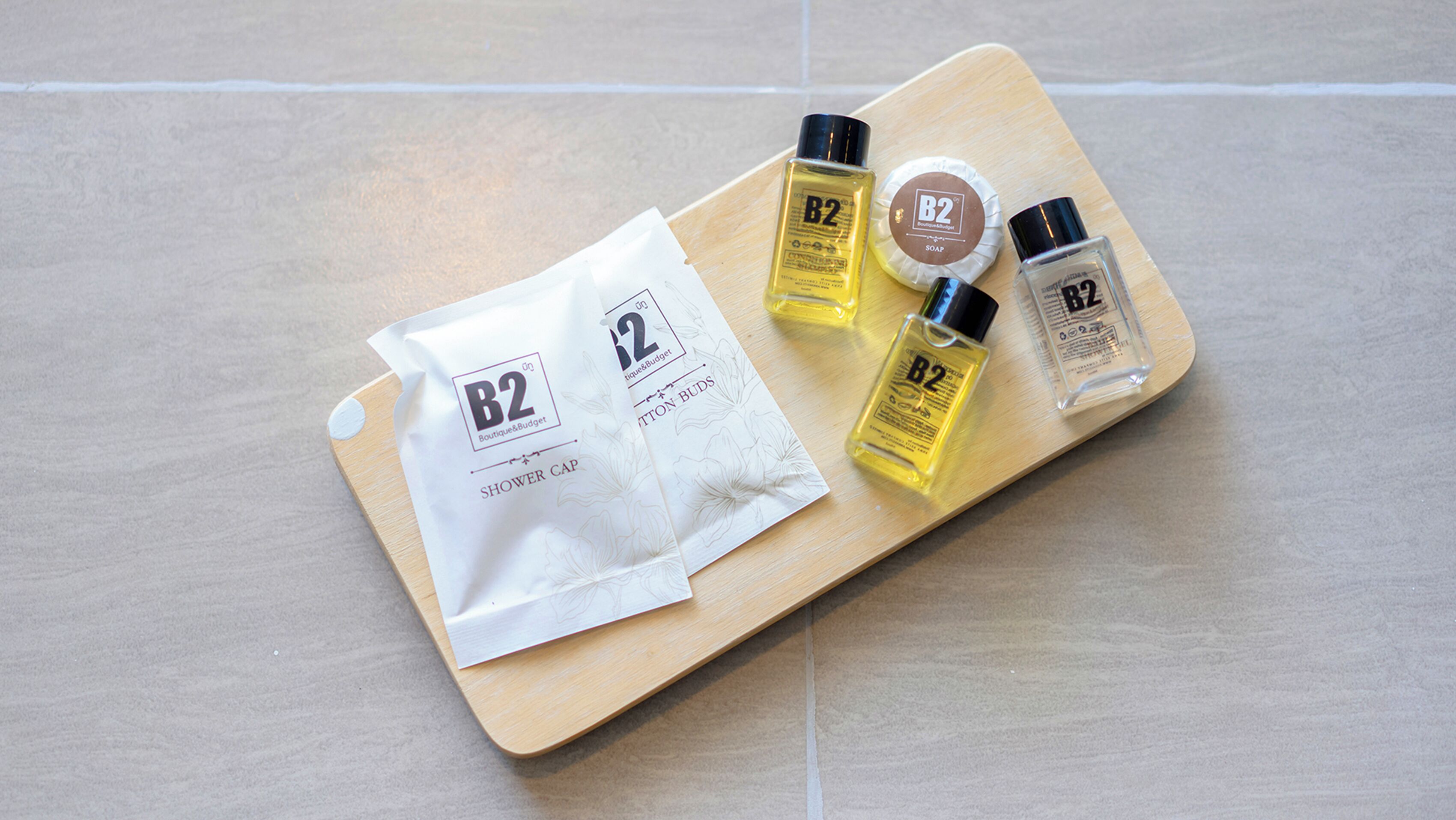 A wooden tray with a white paper bag labeled 'B2 Boutique & Budget' and three bottles of B2 soap.