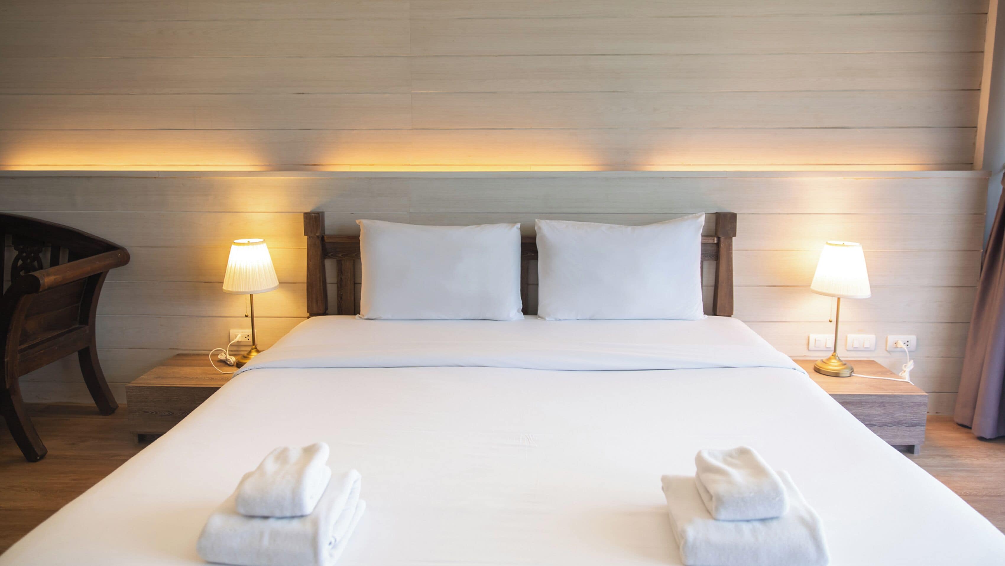Una habitación de hotel con una cama grande, dos lámparas de noche, un cabecero de madera y una silla.