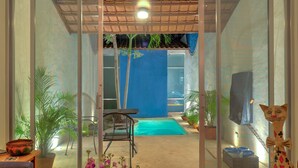 Une porte vitrée donne accès à un espace extérieur abrité, aménagé avec une piscine, des sièges et des plantes en pot.
