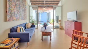 Un salon spacieux avec un canapé bleu, une table basse en bois et un téléviseur posé sur un meuble rose.