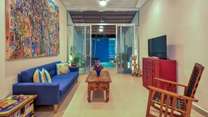 Un salon avec un canapé bleu, une table basse en bois, un meuble rouge et un téléviseur.