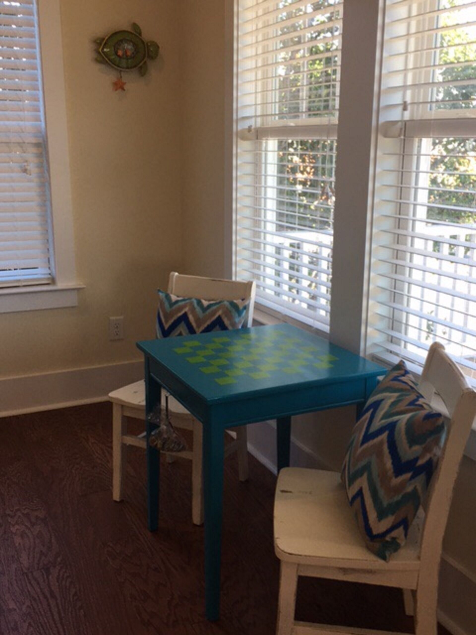 A dining area with a blue table and white chairs, featuring a decorative pillow on one chair.