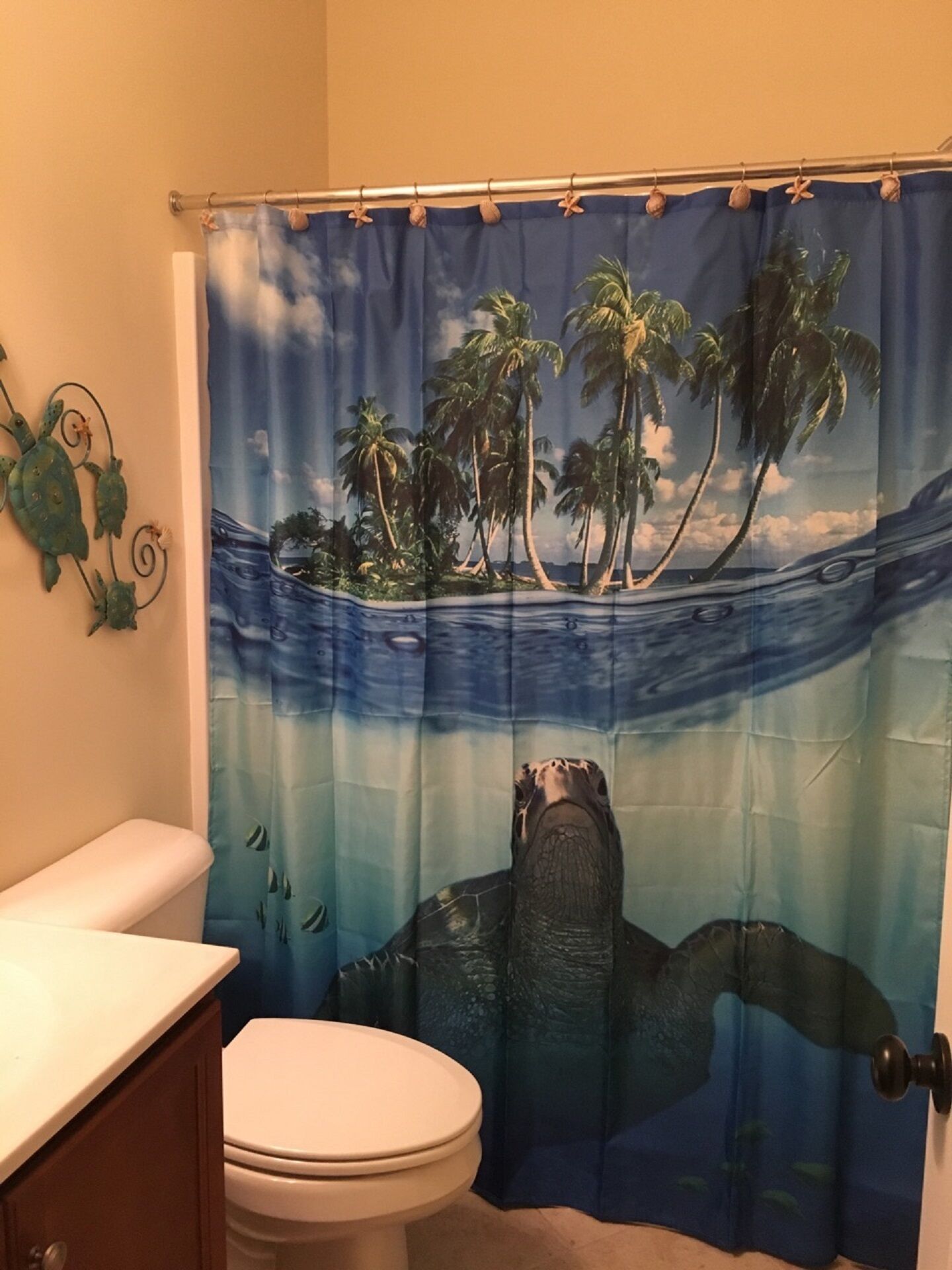 A bathroom with a toilet, a sink, and a shower curtain depicting a sea turtle and palm trees.