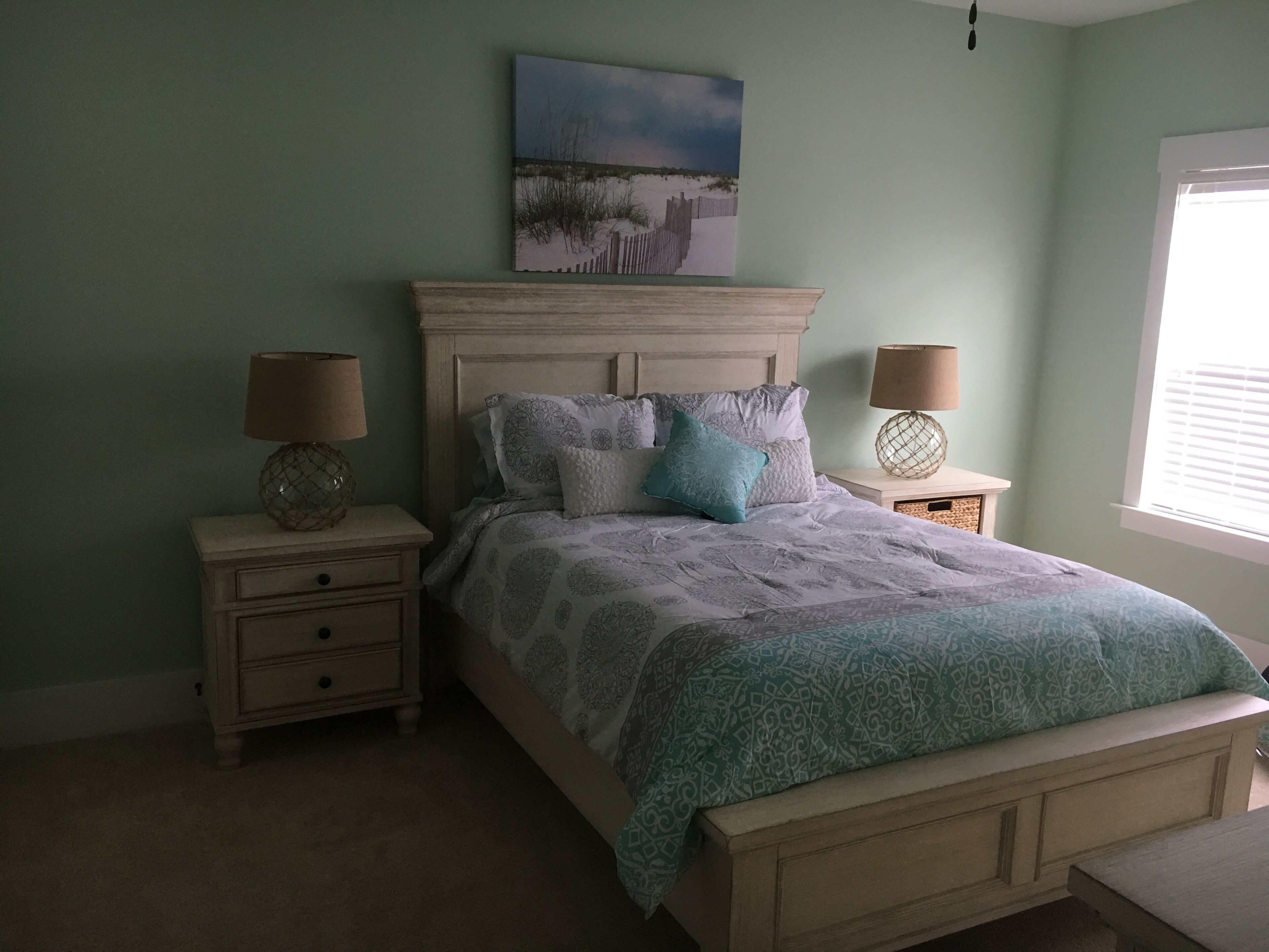A bedroom with a bed, two nightstands, a window, and a painting on the wall.