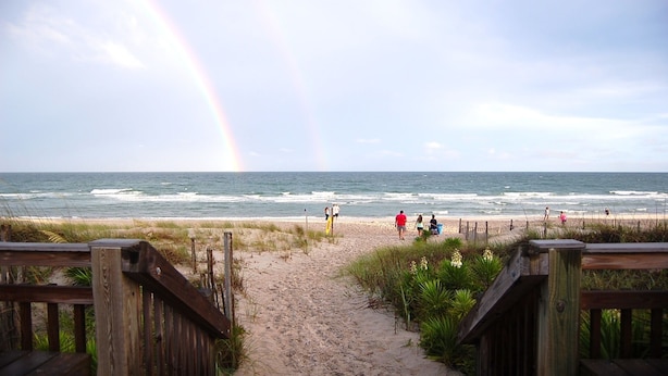Ein Strandweg führt zum Meer, am Himmel ist ein Regenbogen zu sehen.