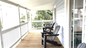 Eine überdachte Veranda mit zwei Adirondack-Stühlen und einem Tisch, Holzboden und einem weißen Geländer.