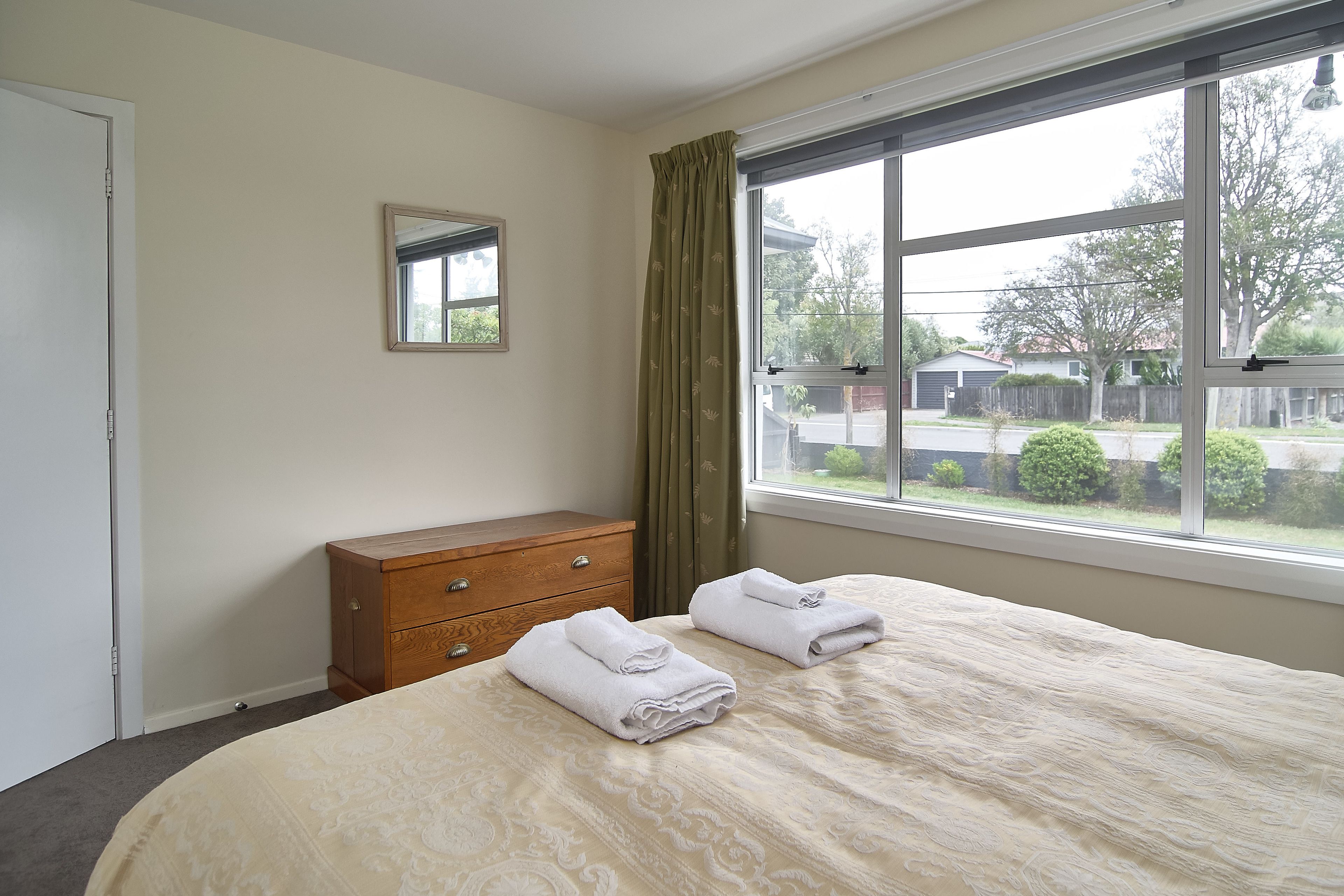 Una habitación de hotel con una cama, un aparador de madera, un espejo y una ventana con cortinas.