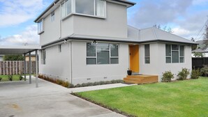 Uma casa moderna de dois andares com varanda coberta, entrada frontal com degraus e gramado bem cuidado.