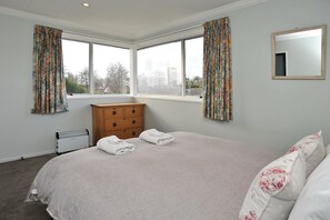 A bedroom with a large bed, a wooden dresser, a radiator, and a window with curtains.