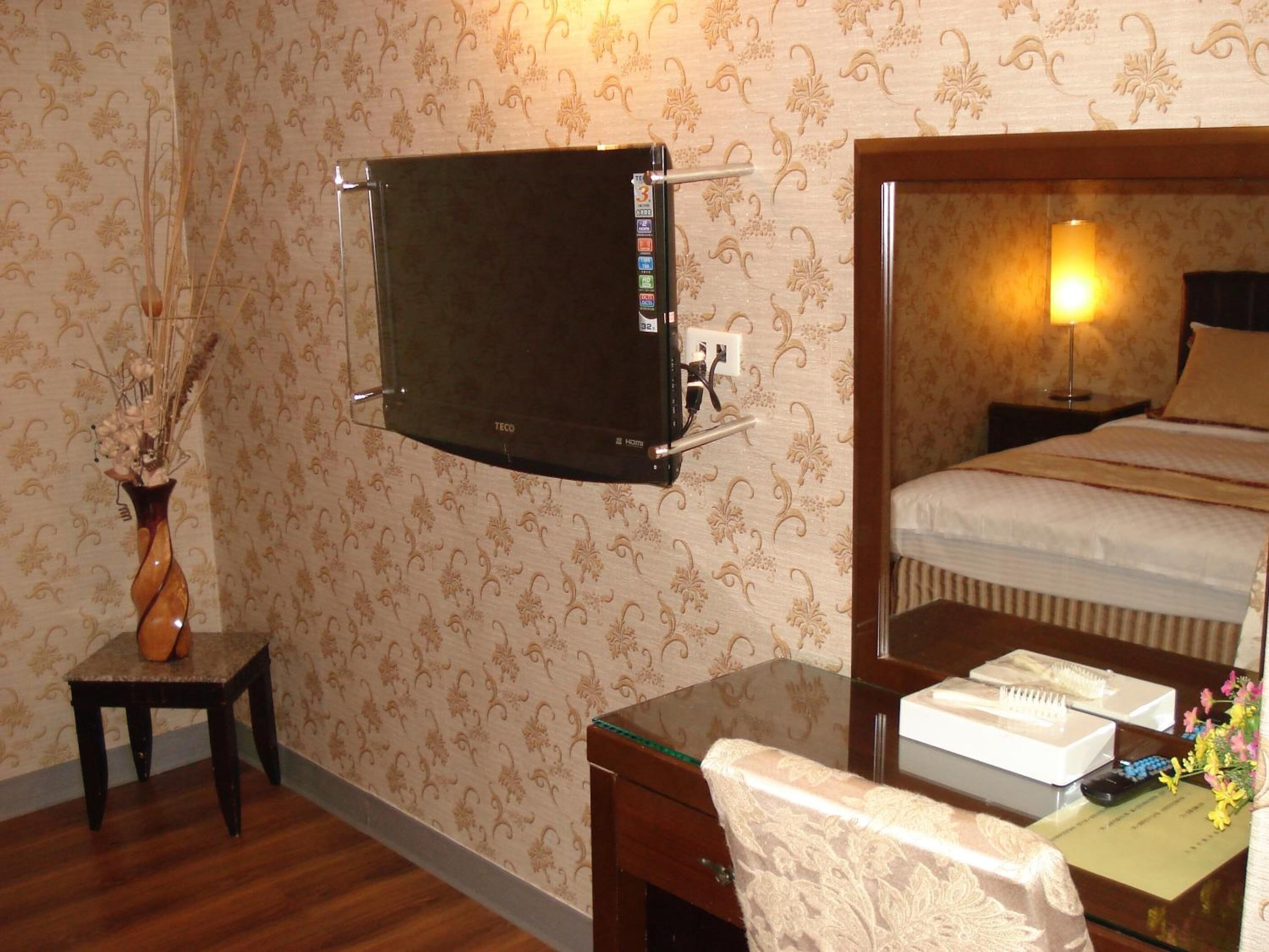 Habitación de hotel con cama, mesita de noche y televisor montado en la pared.