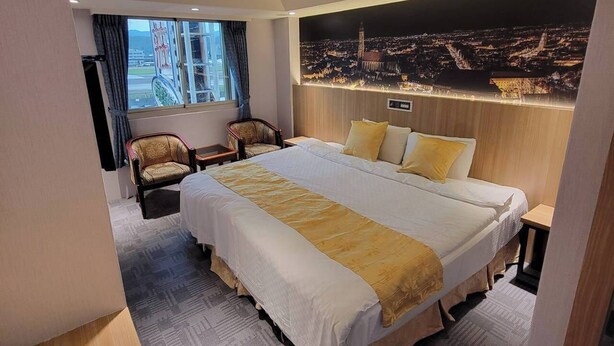 A hotel room with a large bed, a chair, a nightstand, and a cityscape mural on the wall. - Attic Hotel (Taipei)