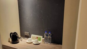 A kitchenette with a coffee maker, two cups, a small fridge, and two water bottles on a wooden countertop. - Attic Hotel (Taipei)