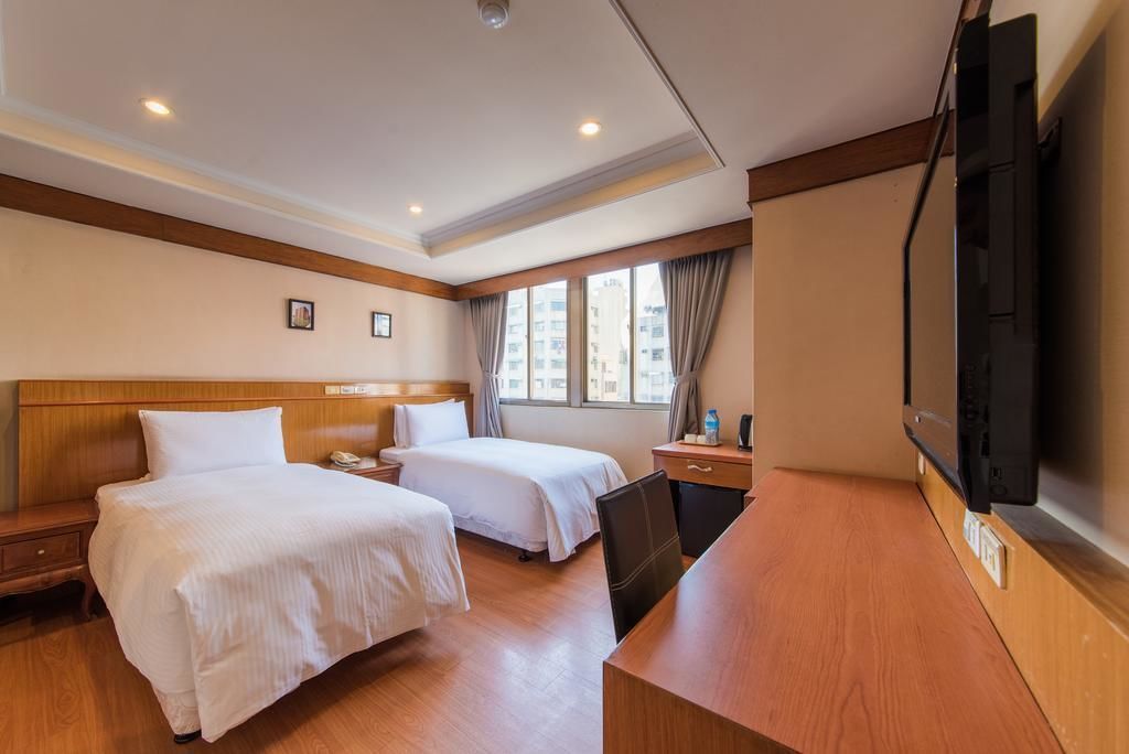 Habitación de hotel con dos camas, un escritorio, un televisor y una ventana con cortinas.