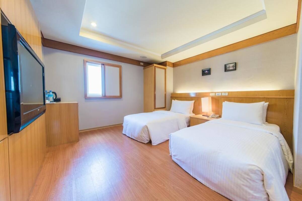 A hotel room with two beds, a TV, a window, and wooden paneling.