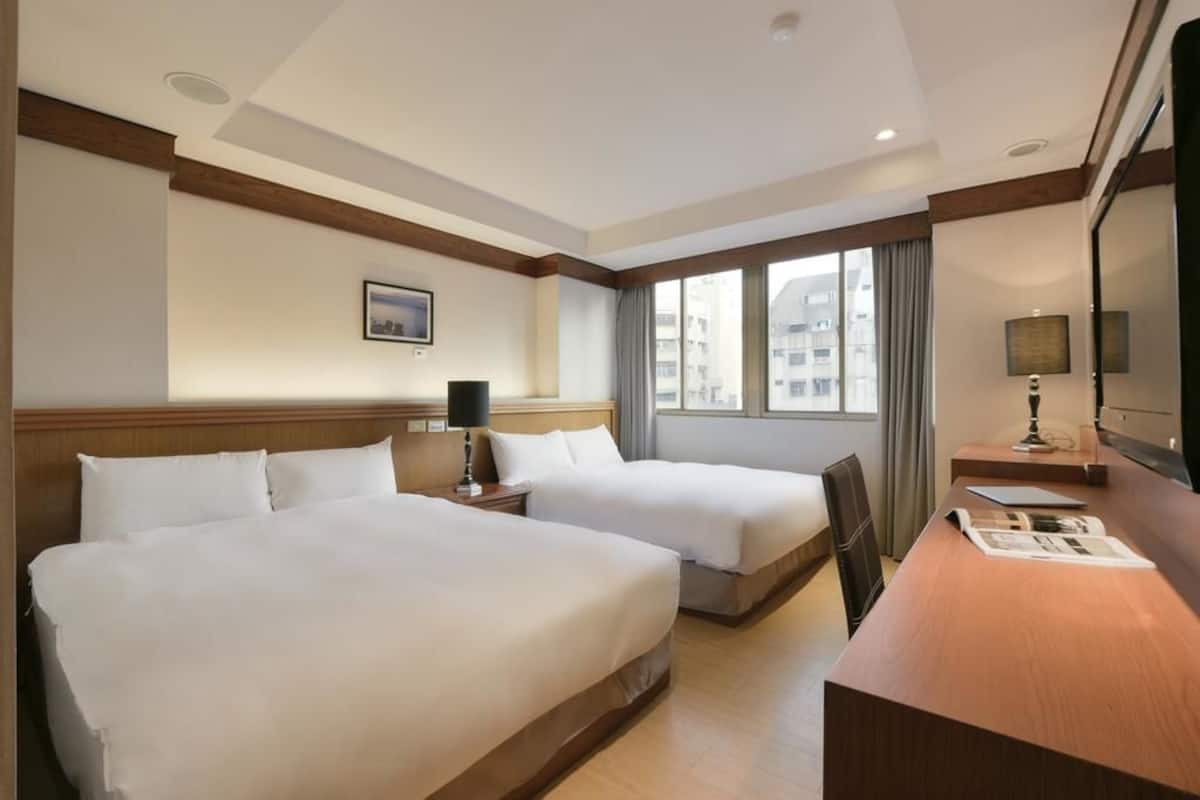 A hotel room with two beds, a desk, and a large window.