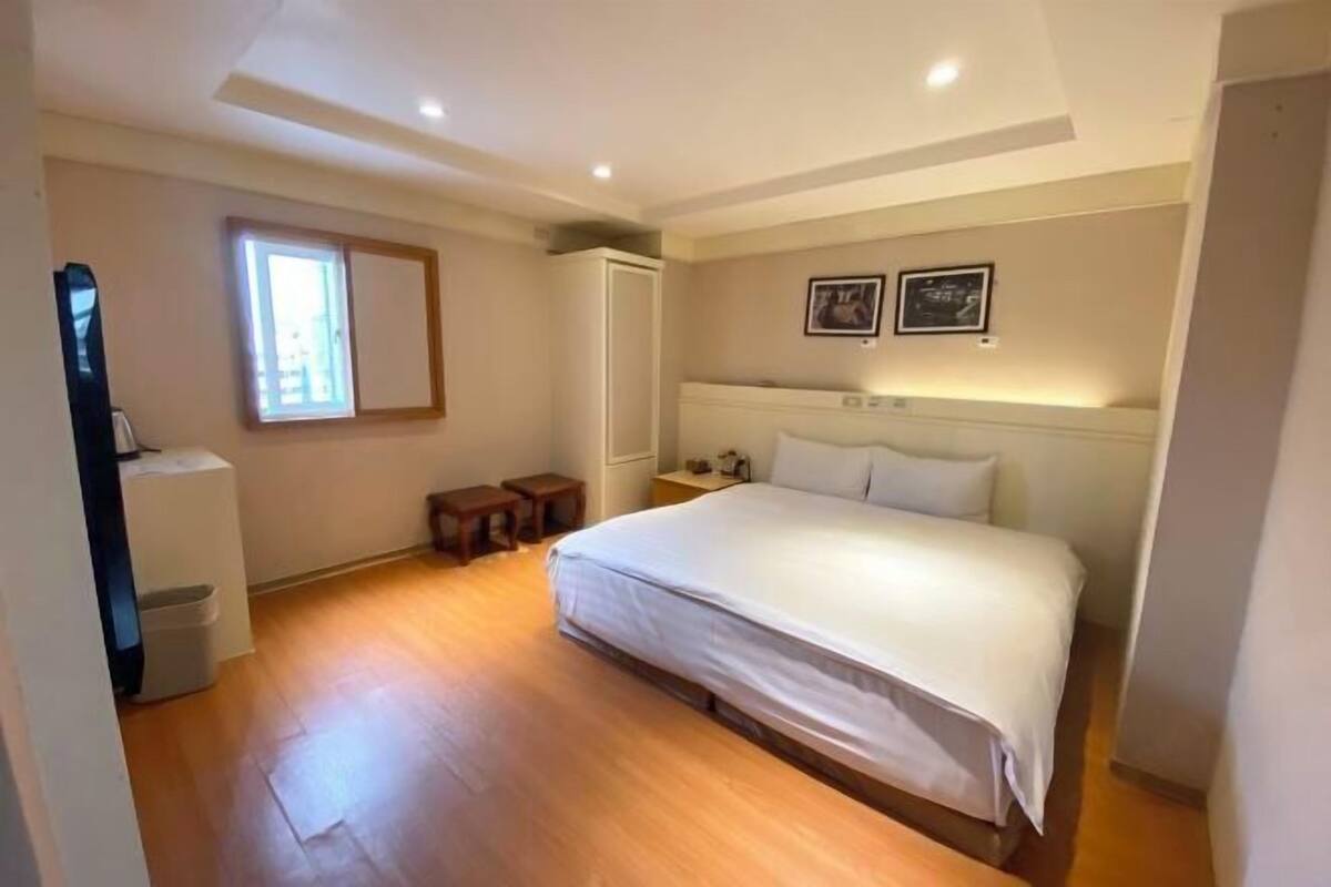 A bedroom with a bed, wooden flooring, a window, a wardrobe, and two bedside tables.