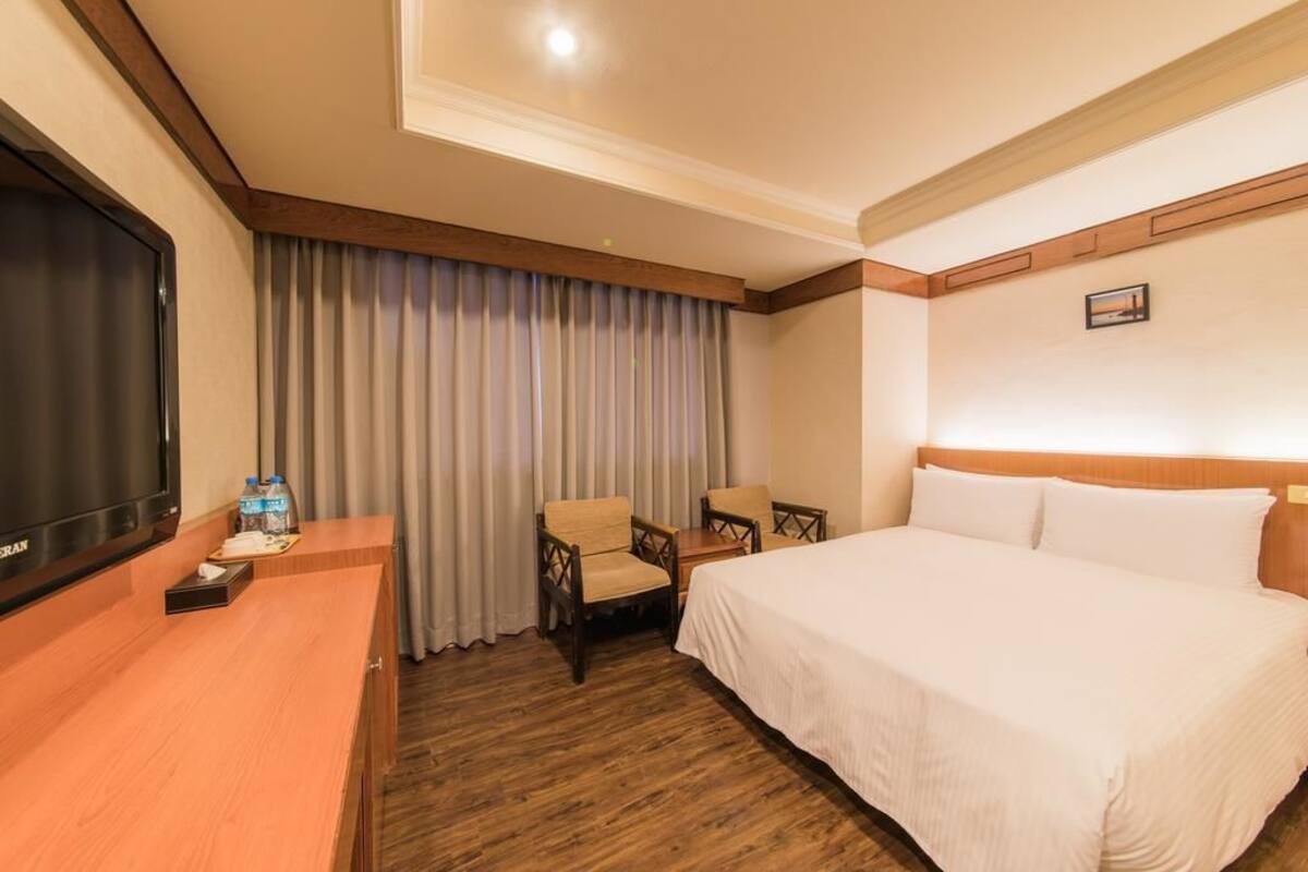 A hotel room with a bed, a TV, a desk with a chair, and a window with curtains.