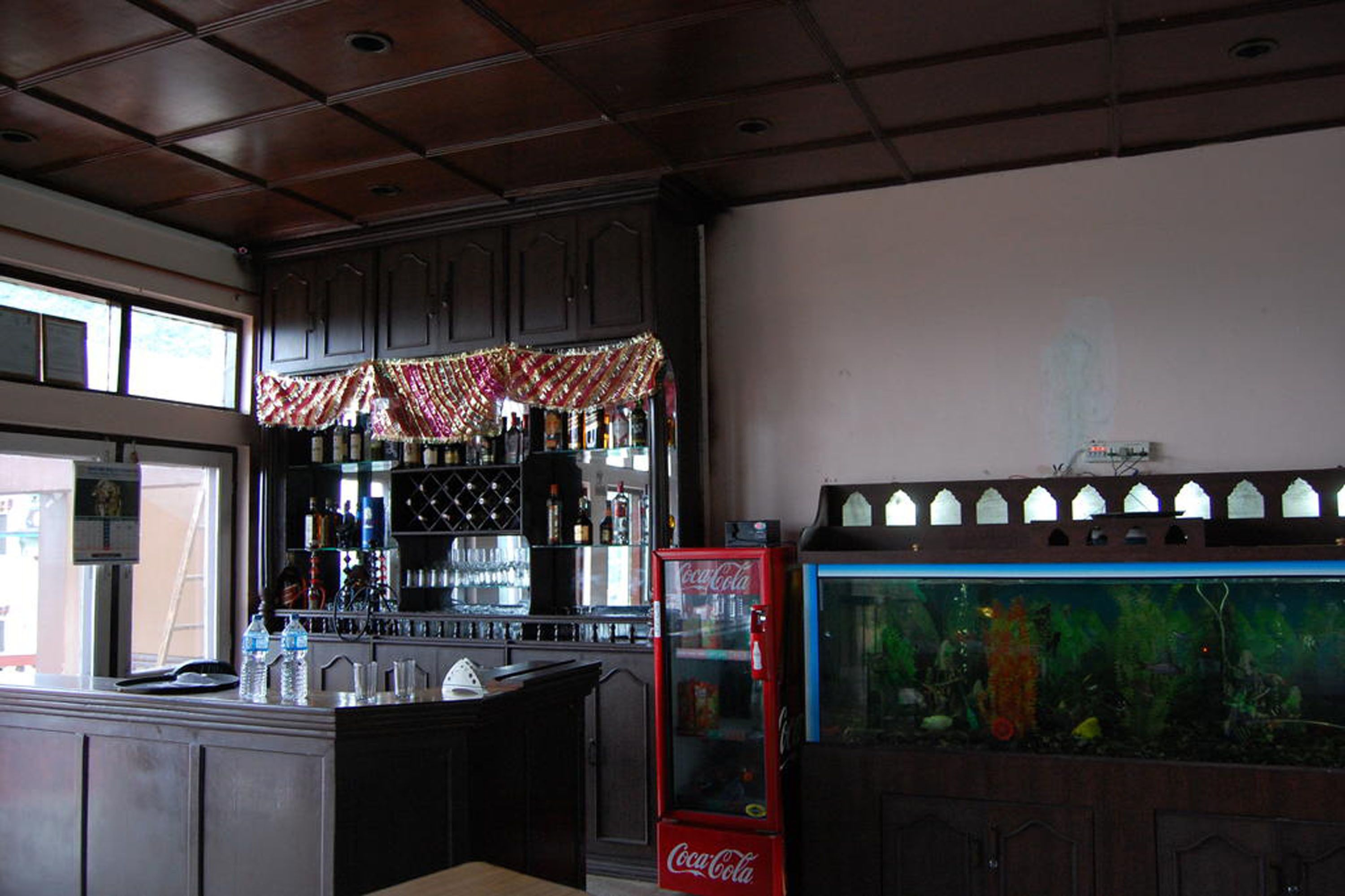 A bar area with a Coca-Cola vending machine, a fish tank, and a bar counter with bottles and glasses.