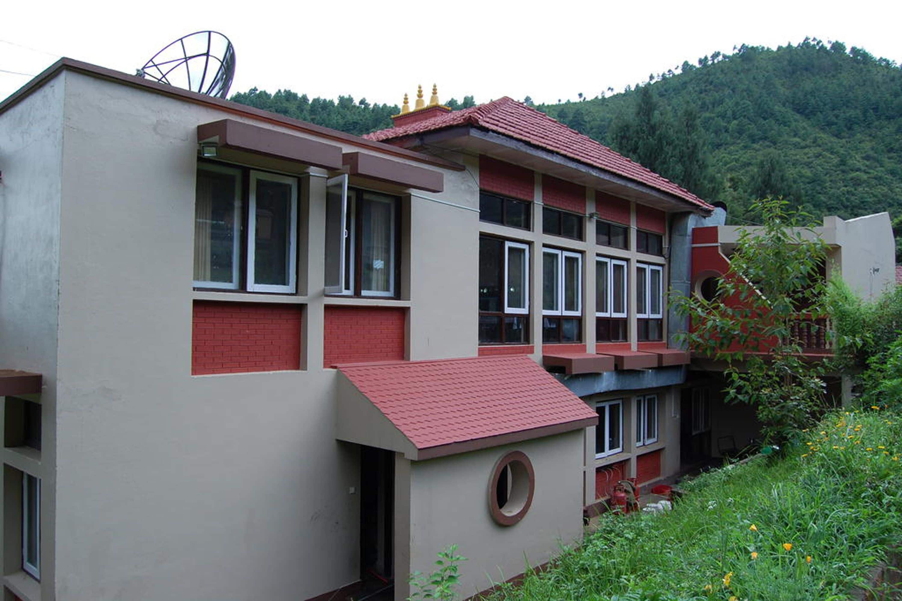 A multi-story building with a red roof, large windows, and a satellite dish on the roof.