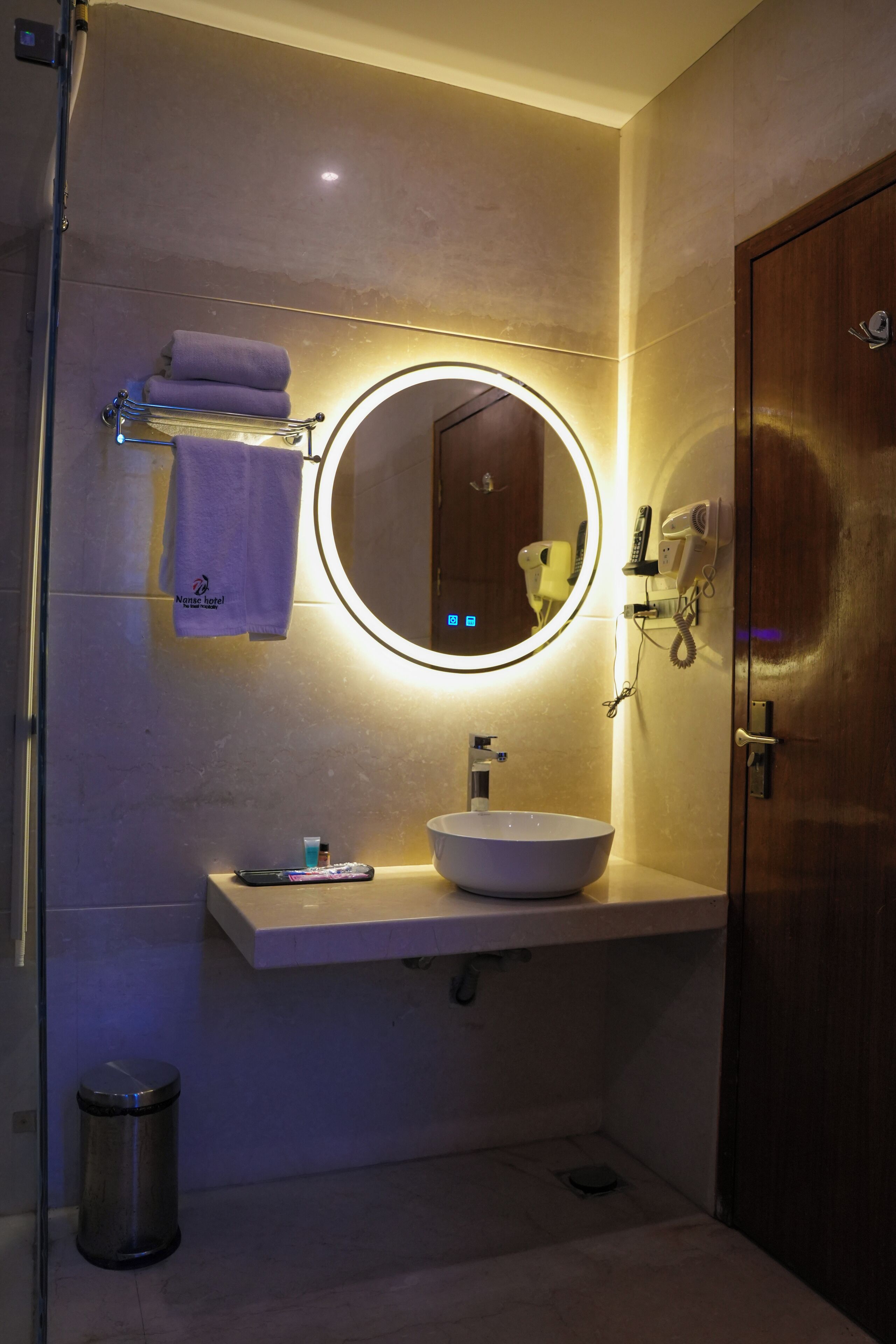 Un baño con un espejo redondo, un lavabo, un secador de pelo y un perchero para toallas.