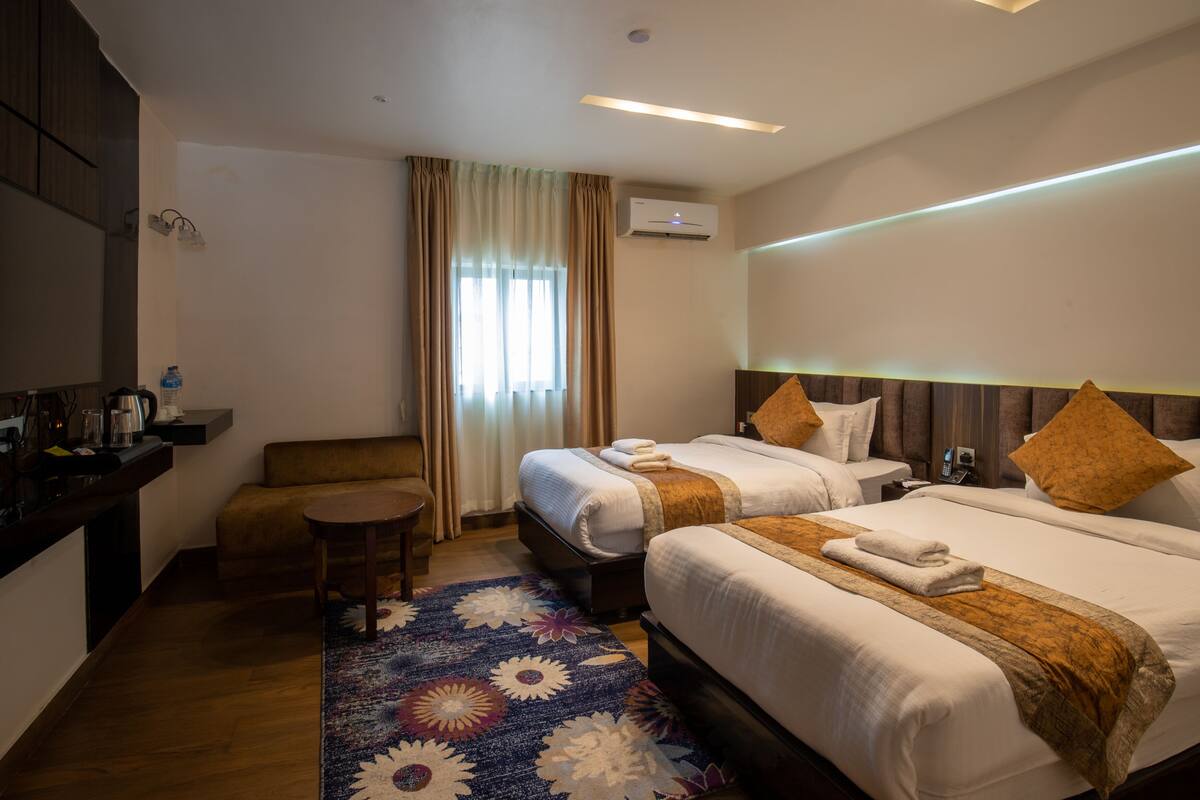 Ein Hotelzimmer mit zwei Betten, einem Schlafsofa, einem kleinen Tisch und einem dekorativen Teppich.