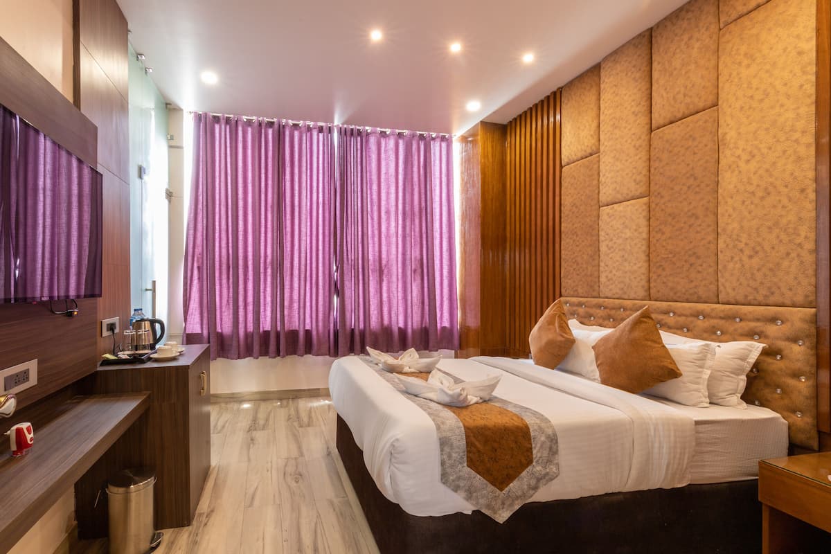 Ein modernes Hotelzimmer mit einem großen Bett, einem Holzkopfstück, einem kleinen Schreibtisch mit Wasserkocher und einem durch einen Vorhang einsehbaren Badezimmer.
