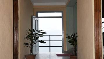 A hallway with a view of a large window, potted plants, and a red carpet.