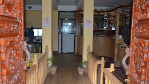 A hotel lobby with a wooden staircase, a reception desk, and a bar area.