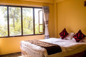 Un dormitorio con un ventanal grande, una cama con ropa de cama blanca y dos almohadas decorativas, y una cortina entreabierta.