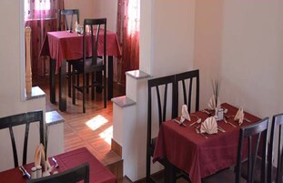 Un comedor con dos mesas, cada una con mantel rojo y sillas.