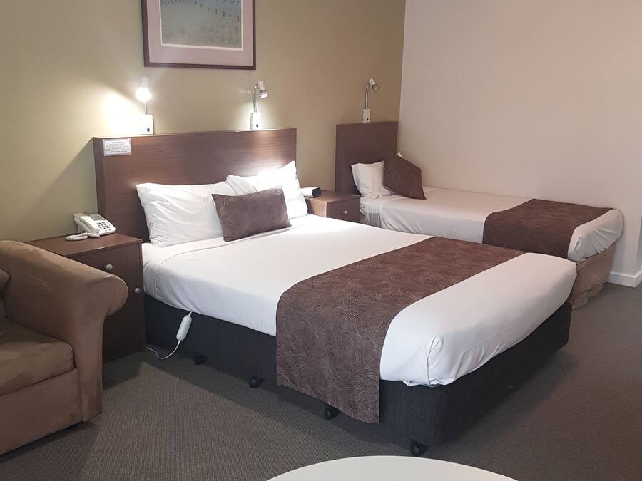 Habitación de hotel con dos camas, un escritorio, una silla, un ventilador de techo y un cuadro en la pared.
