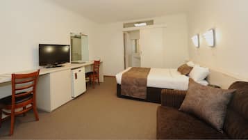 Een hotelkamer met een bed, een bureau met een televisie, een stoel en een kleine koelkast.